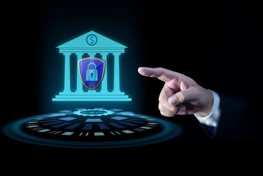 Businessman hand pointing at creative glowing blue bank building hologram with protective shield on dark background. Business, finance and online banking concept