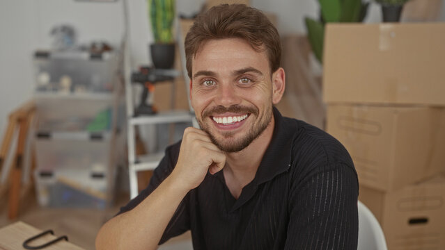 Man smiling with hand on chin in house surrounded by moving boxes and ladder and drill on shelf; moving day optimism.