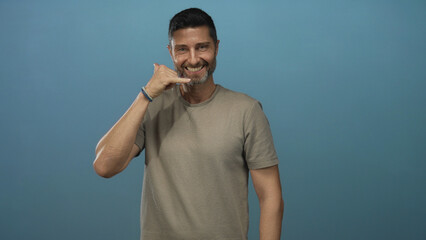 Man hand pointing and hand to ear call gesture in blue studio wall, smiling and engaging with camera; friendly invitation.