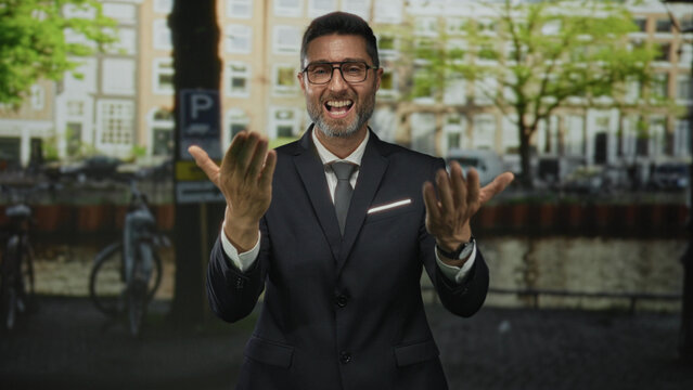 Man in suit points finger to camera showing hands on street by canal in amsterdam; confidence approachability success.