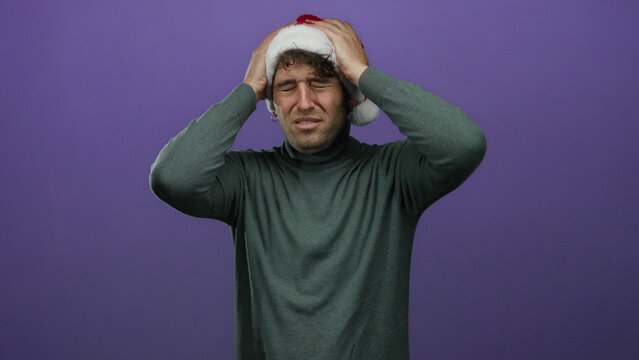 Hispanic man in christmas hat holds head with frustrated expression against purple background representing holiday stress and seasonal emotions - Powered by Adobe
