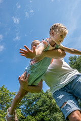 Father lifting daughter joyfully in a sunny park, showcasing their playful bond and happiness, capturing the essence of childhood and family love in a vibrant outdoor setting © Silga