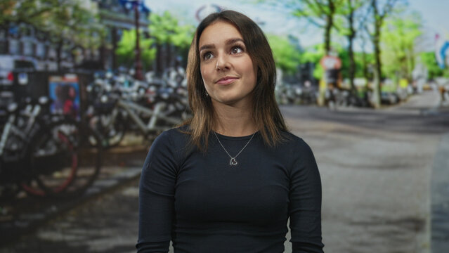 Woman wearing heart pendant looks up on an amsterdam street with bicycles and trees; quiet curiosity.
