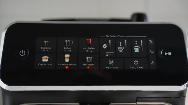 A finger selects a drink on a bean-to-cup machines touchscreen. Menu shows espresso, coffee, iced coffee, and milk drinks.