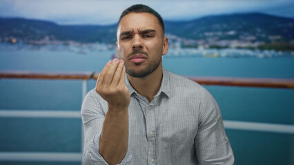 Young hispanic man with pinched fingers gesture and raised hands on street outdoors; uncertainty.