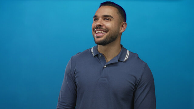 Man smiling with bare teeth in studio with upward gaze and open posture against blue backdrop; happiness.
