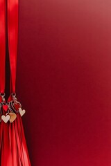 Red ribbons with heart charms on a dark red background with copy space