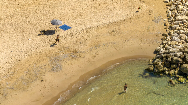 Aerial view of people vacationing on a sandy beach. Tourists have parasols and the sea is emerald green.