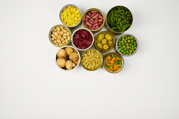 Open cans of beans, mushrooms, carrots, corn, peas, green beans, lentils, asparagus, and olives on a white background with copy space.