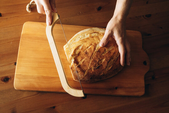 Hands slicing warm sourdough loaf on wooden cutting board  