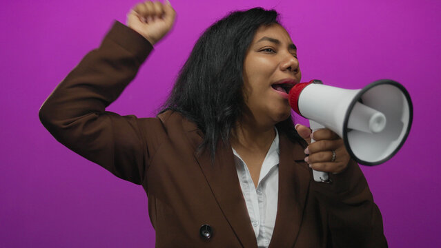 African american woman shouts into megaphone while pointing finger upward in purple studio; confidence.