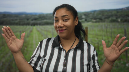 Obraz premium Woman referee in striped shirt smiles and raises palms gesture with whistle at neck in forest clearing; serenity.