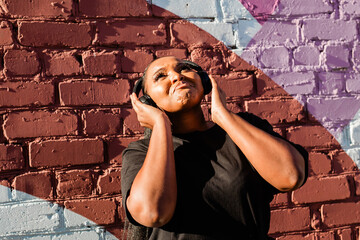 African american woman dancing playfully with headphones against painted wall. Concept of joy, energy, fun and youth lifestyle.