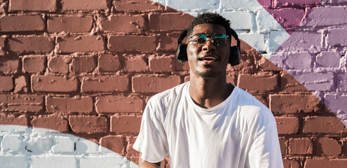 Young african american man dancing with headphones on colorful wall background. Concept of music, joy, freedom and urban lifestyle. Copy space banner