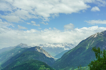 Obraz premium A mountainous alpine landscape in France in summer, the mountains are green with some patches of snow, the sky is blue and clear with a few clouds