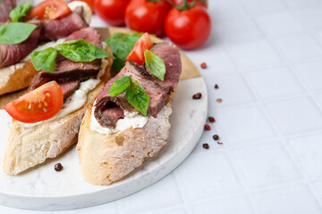 Delicious bruschettas with roast beef served on white tiled table, closeup. Space for text
