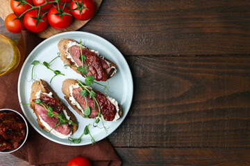 Delicious bruschettas with roast beef served on wooden table, flat lay. Space for text