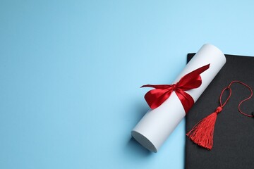 Diploma and graduation hat on light blue background. Space for text