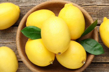 Fresh lemons with green leaves and bowl on wooden table, flat lay
