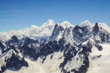 A range of jagged, high alpine mountains in Chamonix France View from the Aiguille du Midi mountain There is snow on the mountains, the sky is blue, and some clouds are visible
