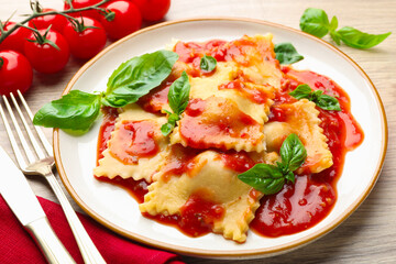 Delicious ravioli with tomato sauce and basil served on light wooden table, closeup