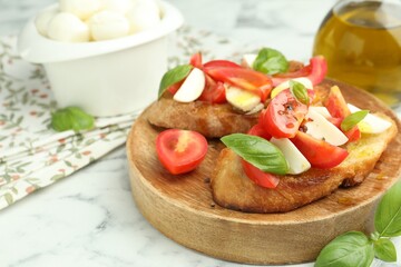 Tasty bruschettas with mozzarella cheese, tomatoes and basil on white marble table, closeup