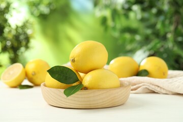 Fresh lemons with green leaves on white wooden table outdoors, closeup