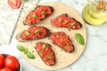 Tasty bruschettas with tomatoes, basil and oil on white marble table, flat lay
