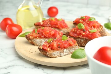Tasty bruschettas with tomatoes and basil on white marble table, closeup