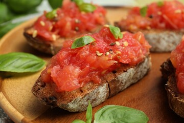 Tasty bruschettas with tomatoes and basil on wooden board, closeup
