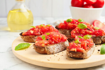 Tasty bruschettas with tomatoes and basil on white marble table, closeup