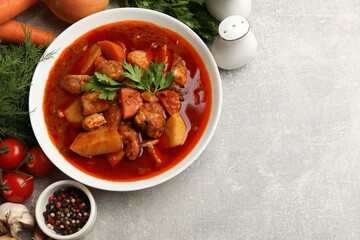 Delicious cooked stew in bowl and fresh ingredients on grey table, flat lay. Space for text