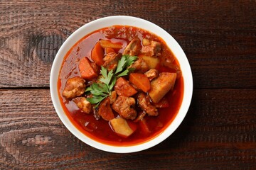 Delicious cooked stew in bowl on wooden table, top view