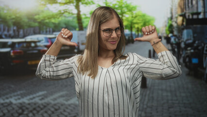 Fototapeta premium Woman smiling and pointing thumb at herself on a cobblestone street lined with parked cars and bicycles; confidence empowerment pride selfbelief.