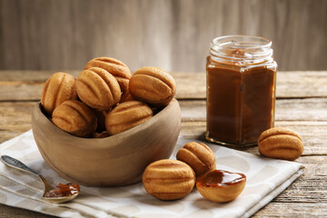 Tasty nut shaped cookies with boiled condensed milk on wooden table, closeup