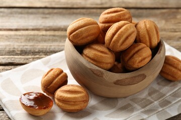 Delicious nut shaped cookies with boiled condensed milk in bowl on wooden table, closeup