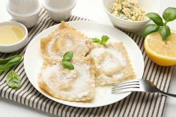 Delicious ravioli with cream sauce and basil served on white table, closeup