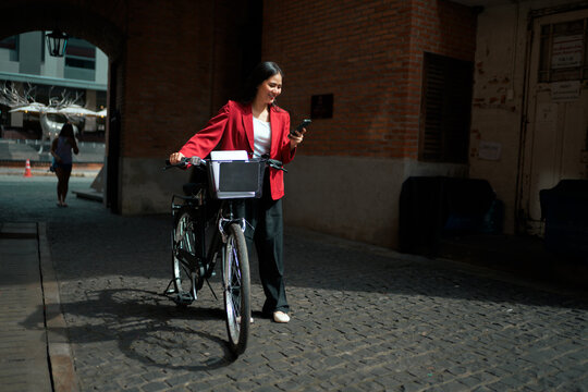 Businesswoman walking bicycle, checking smartphone in city