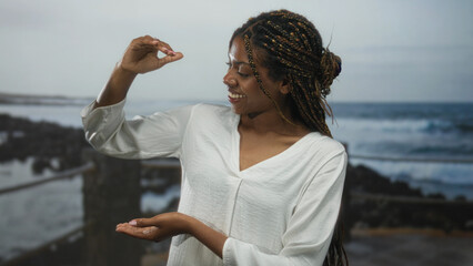 African american woman in white blouse holding hands apart as if measuring an object at beach; serenity.