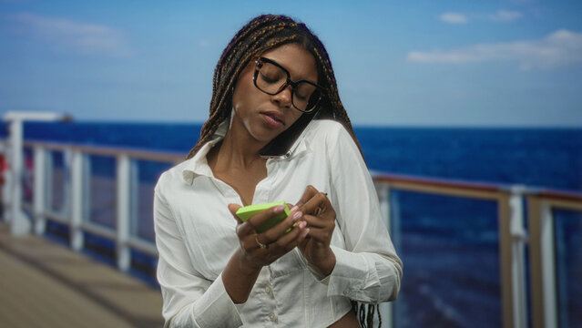 Woman holding smartphone between shoulder and ear while writing on a green notepad with a pen on a cruise ship deck near railing on a street; concentration travel planning.