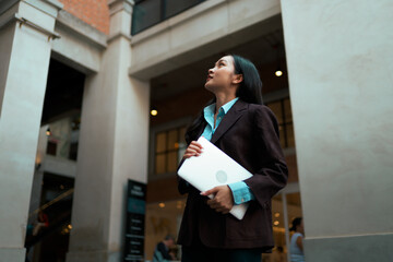 Asian businesswoman with laptop looking up in urban environment © Parichat