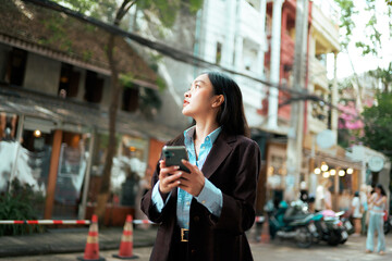 Asian businesswoman using phone and looking up in urban city street