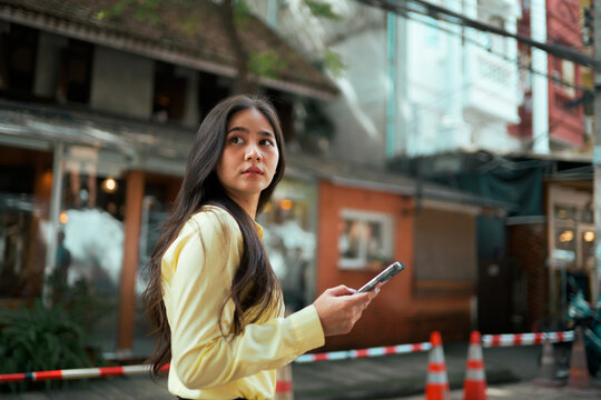 Young Asian woman holding phone navigating city street