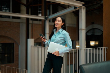 Fototapeta premium Asian businesswoman multitasking, holding laptop and smartphone in modern office
