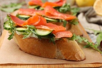 Tasty bruschettas with salmon, cucumber and arugula served on table, closeup