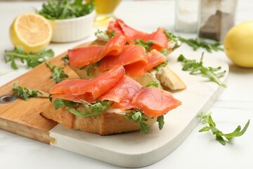 Tasty bruschettas with salmon and arugula served on white table, closeup