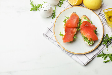 Tasty bruschettas with salmon and arugula served on white marble table, flat lay. Space for text
