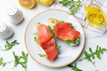 Tasty bruschettas with salmon and arugula served on white marble table, flat lay