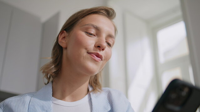 Relaxed lady messaging cellphone in sunny kitchen. Closeup pretty girl dreaming 