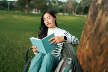 Fototapeta premium Young woman student reading book in green park